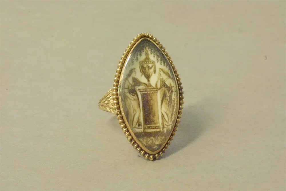 A gold mourning ring featuring a painting on ivory of two women with a funerary urn.