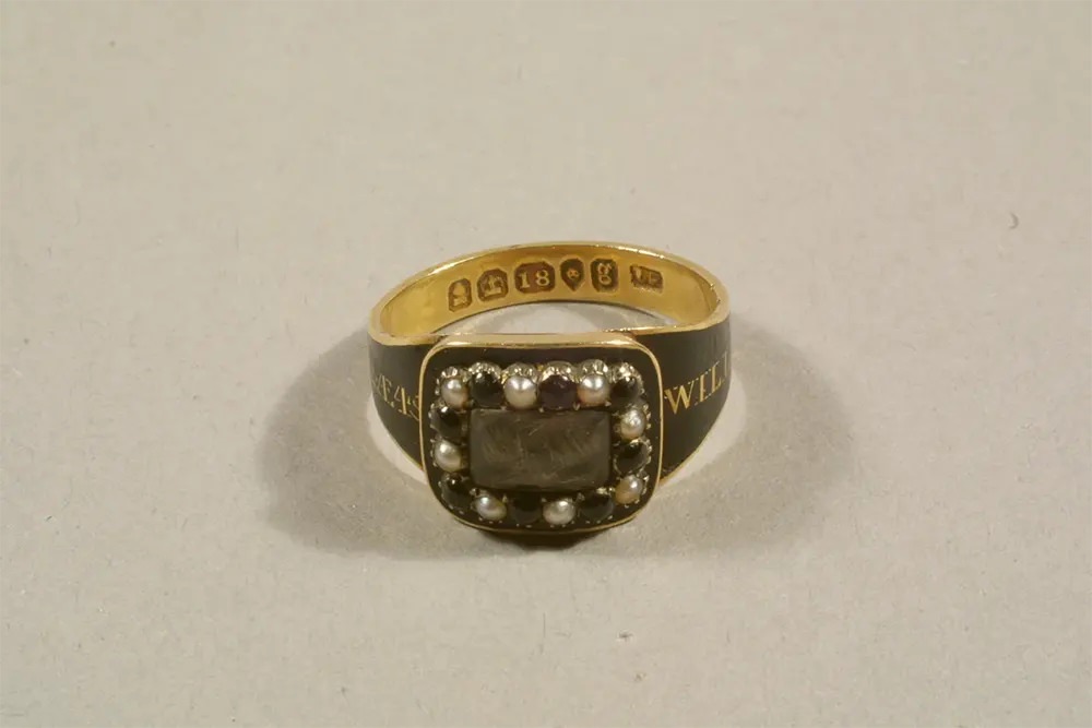 A gold and black mourning ring with a plait of the deceased’s hair set under glass.