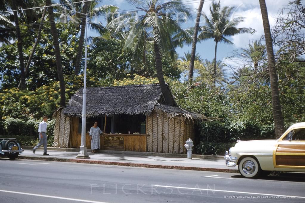 Aunty Bella’s lei stand on Waikiki’s Kalakakaua Avenue Street frontage at the Royal Hawaiian Hotel before the parking meters went in, 1952