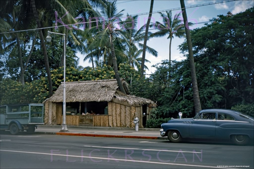 Aunty Bella’s lei stand on the makai (ocean) side of Waikiki’s Kalakaua Avenue after the parking meters went up 1953