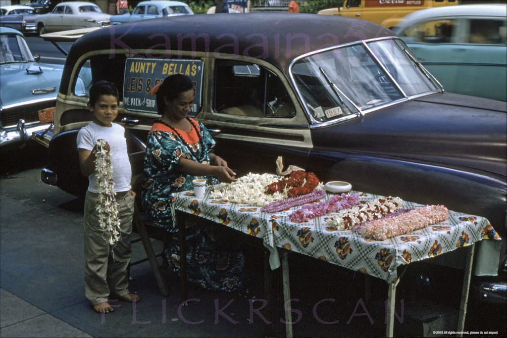 Aunty Bella’s sidewalk lei stand in its usual spot on Kalakaua Avenue across from the Waikiki Theatre, 1957