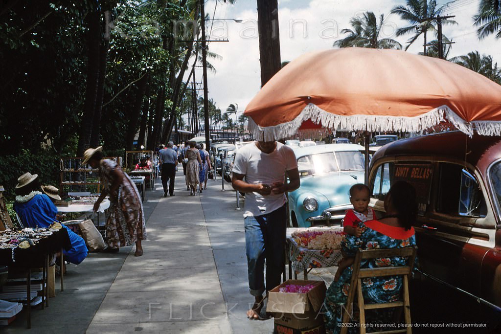 Local vendors selling fresh lei and souvenirs along the makai side of Waikiki’s Kalakaua Avenue in front of the Royal Hawaiian Hotel, 1958