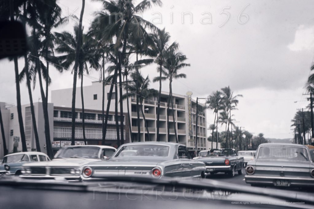 Heading Ewa (west) Waikiki’s along busy Kalakaua Avenue at the intersection with Beach Walk, 1964