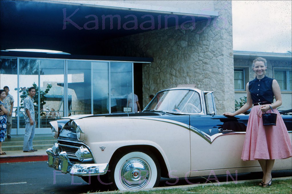 Pretty young lady in pink and black styling beside a pink and black Ford Sunliner convertible in front of the Waikiki Aquarium, 1956
