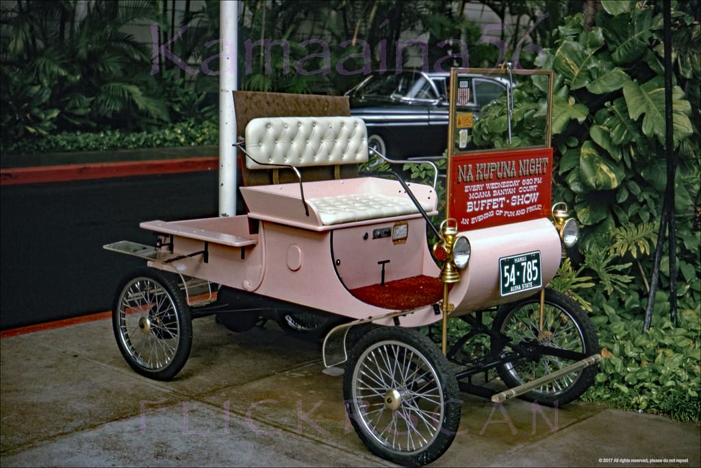 Oldsmobile Model R Curved Dash Runabout on the sidewalk in front of Waikiki’s Moana Hotel Advertising Na Kupuna (the elders) Night Wednesdays in the Banyan Court, 1962
