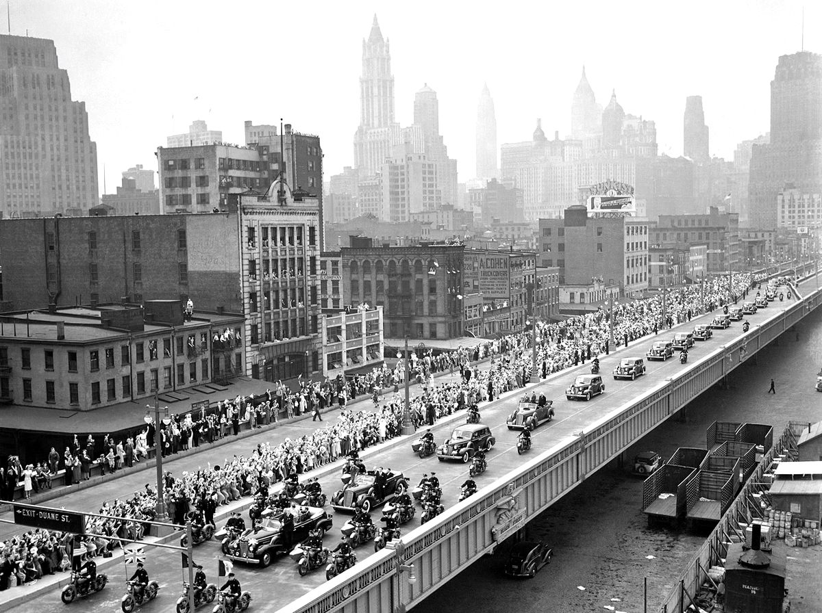 With New York City as a backdrop, King George VI and Queen Elizabeth (first car) proceed up the Westside highway along the Hudson en route to the New York World's Fair.