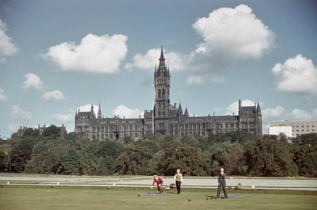 Three men play a game of lawn bowls on a bowling green in West End Park with the New Buildings of the University of Glasgow rising behind on Gilmorehill in Glasgow, 1965.