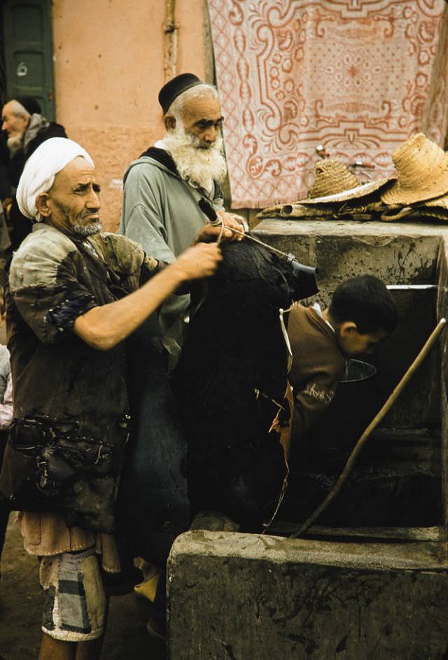 Man filling animal skin with water front fountain in Marrakech, 1960s