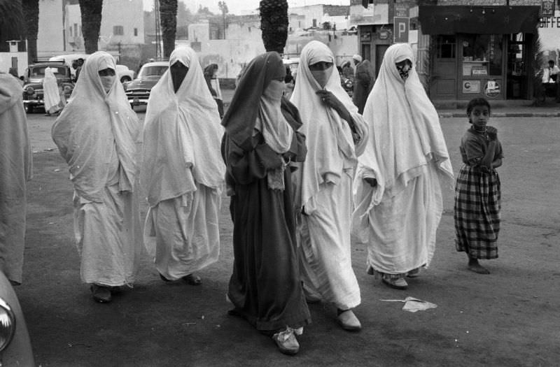 Women in niqabs and abayas walking in street, 1960s