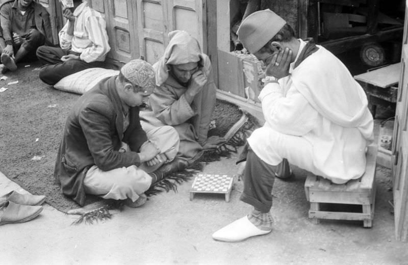 Men playing checkers on sidewalk in front of shop, 1960s