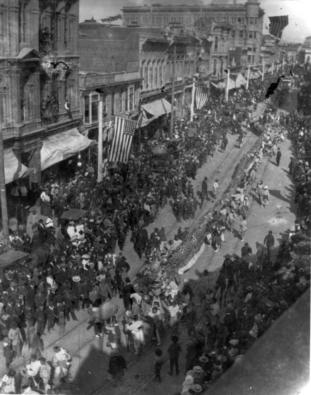 Downtown Bakersfield during a holiday parade, 1907. Shows buildings, crowd, American flags, Chinese-American portion of the parade.