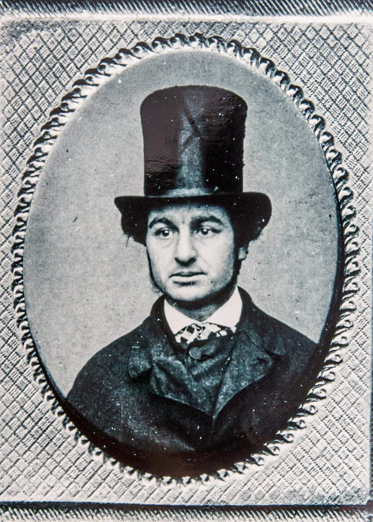 Mugshot of an unknown man in a rather fetching stovepipe hat.