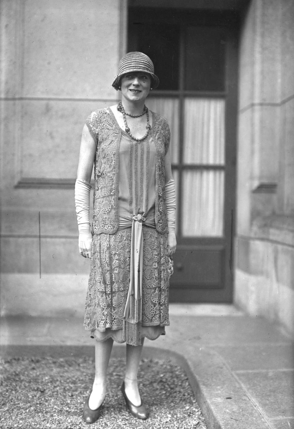 Lace dress with a sash knotted at the hips and a scalloped hem, with matching tunic and a straw cloche hat, set off by a pair of elbow length gloves, 1925