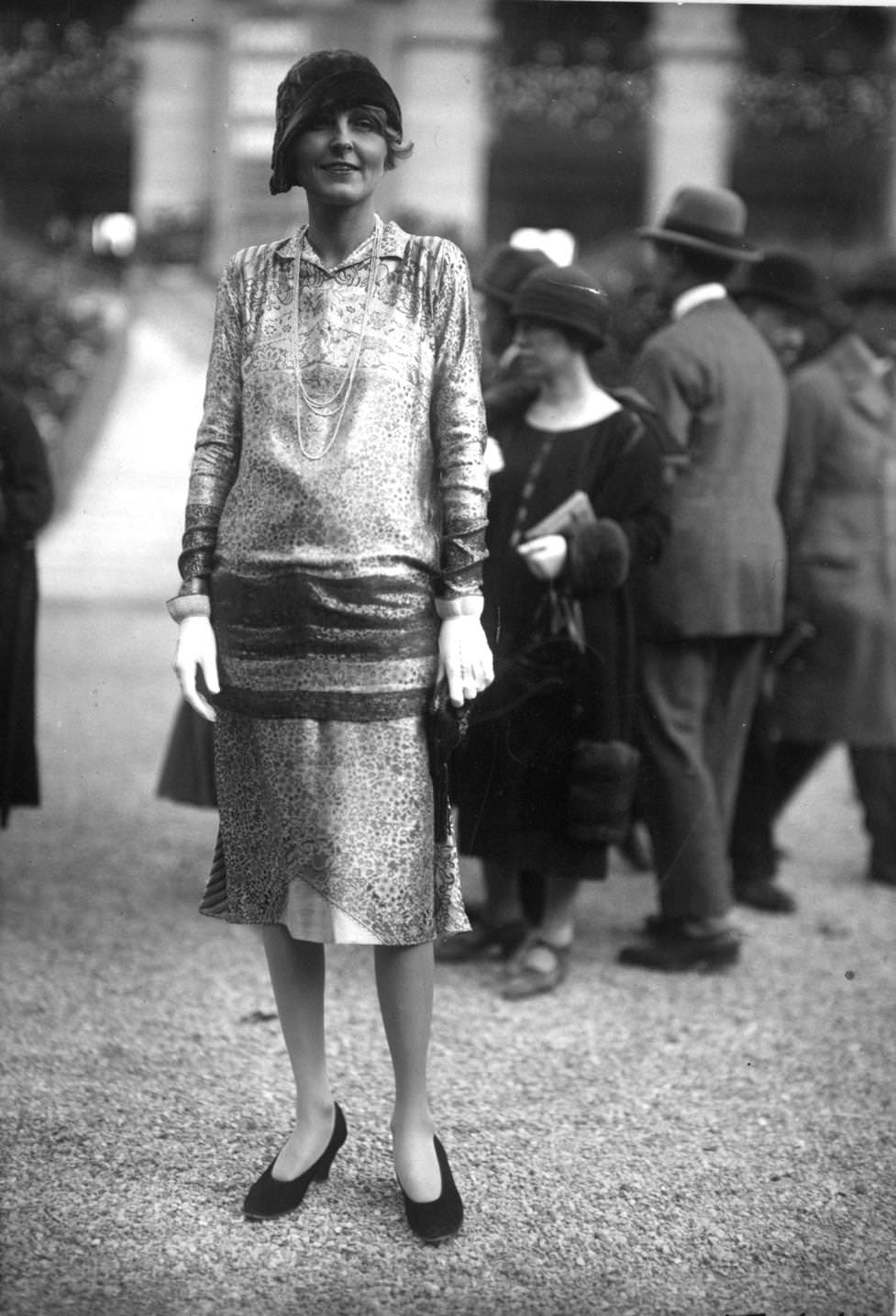 Long-waisted dressworn with an aymmetrical cloche hat and plain court shoes. Ropes of beads complete the outfit, 1925