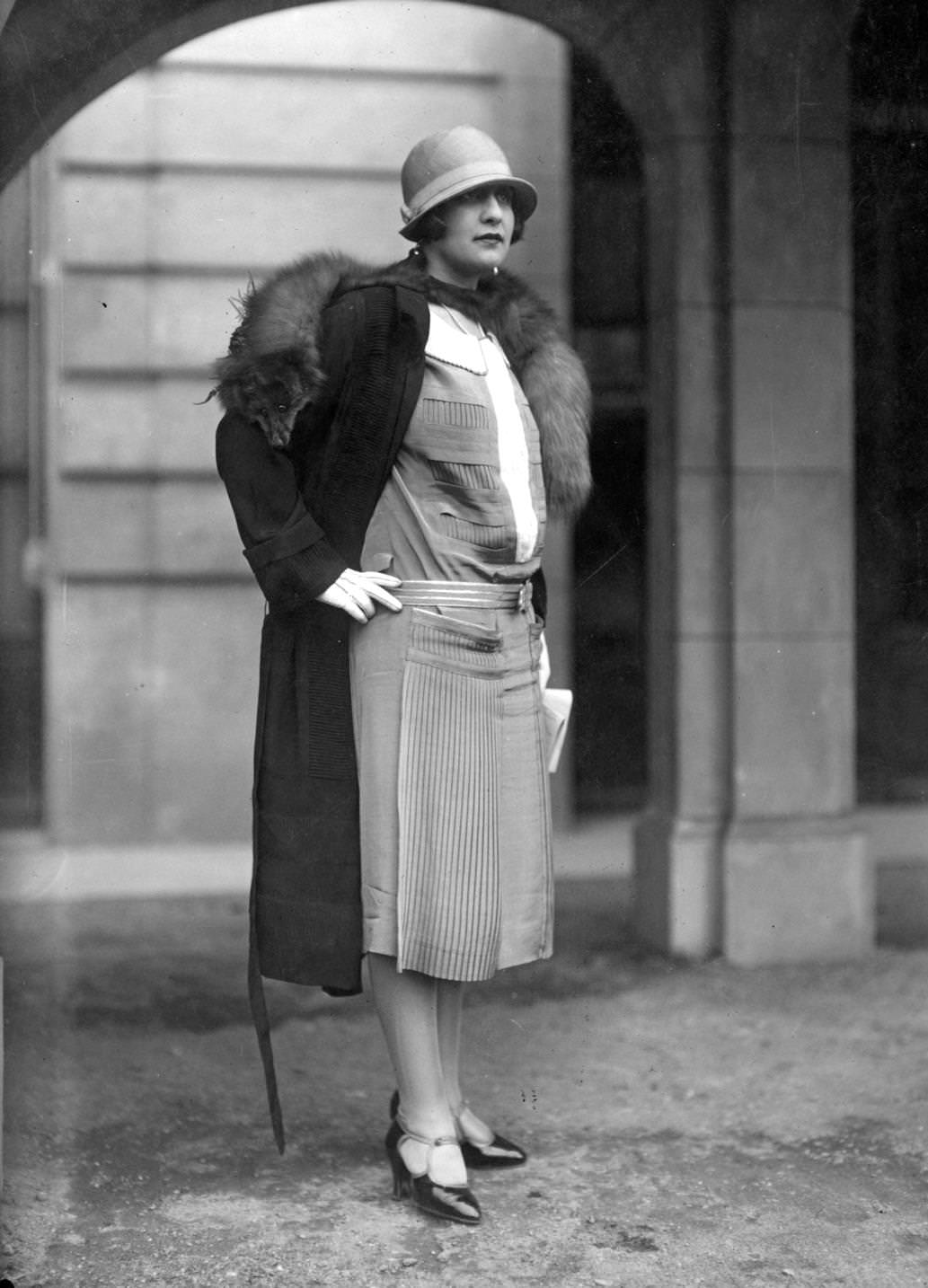 Dress with pleated panels worn with a coat and fox fur and a small brimmed cloche-hat, 1925.