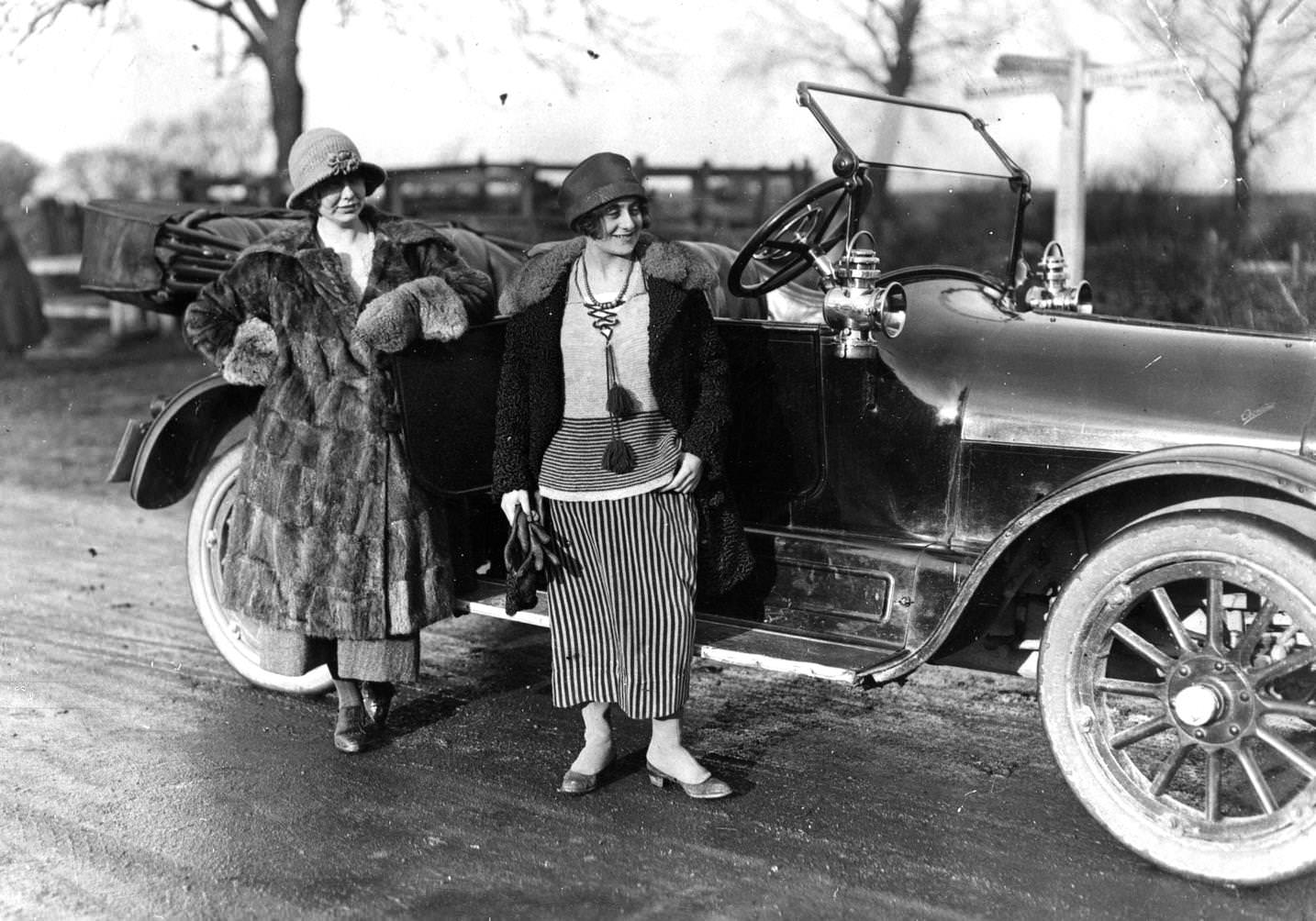 Two ladies, wearing fur coats and Cloche Hat, on their way to a hunting meet, standing by their convertible car.