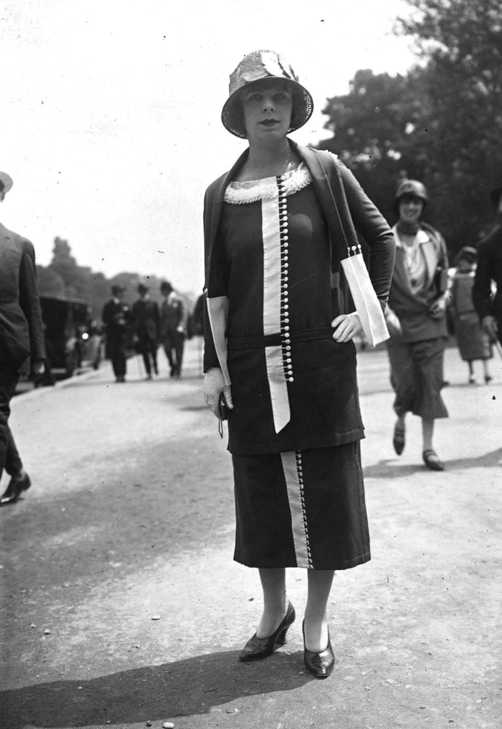 Long-sleeved tunic dress with a boat neck and matching scarf, skirt and top are decorated with contrasting cloth buttons . A hat is a deep crowned straw cloche decorated with leaves, 1924