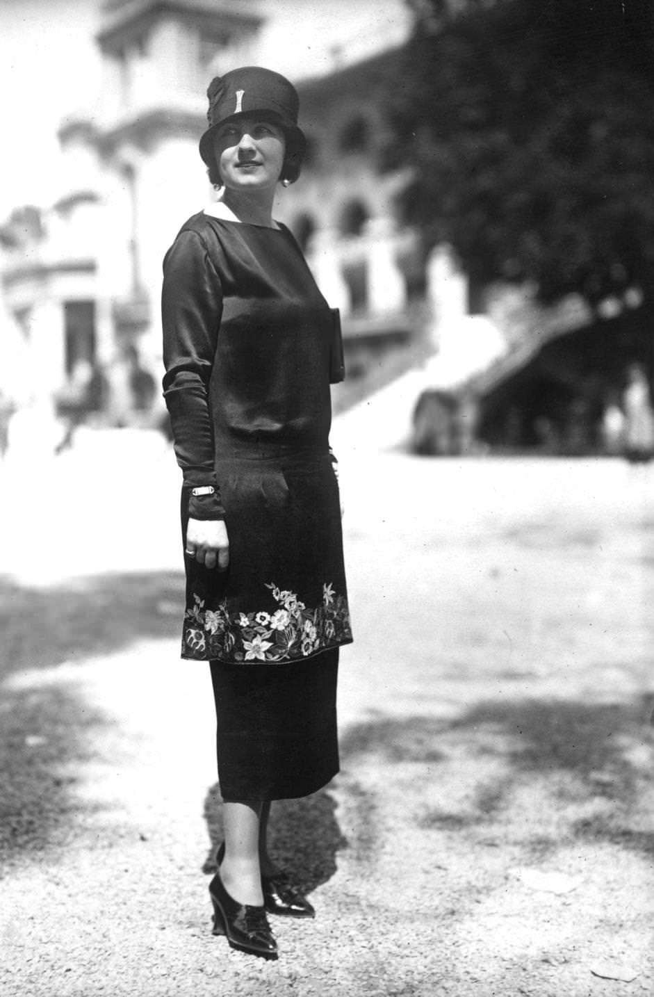 A tunic dress with embroidery round the edge of the tunic, high cut court shoes and a deep crowned cloche hat complete an outfit designed by Marie-Alys, 1924