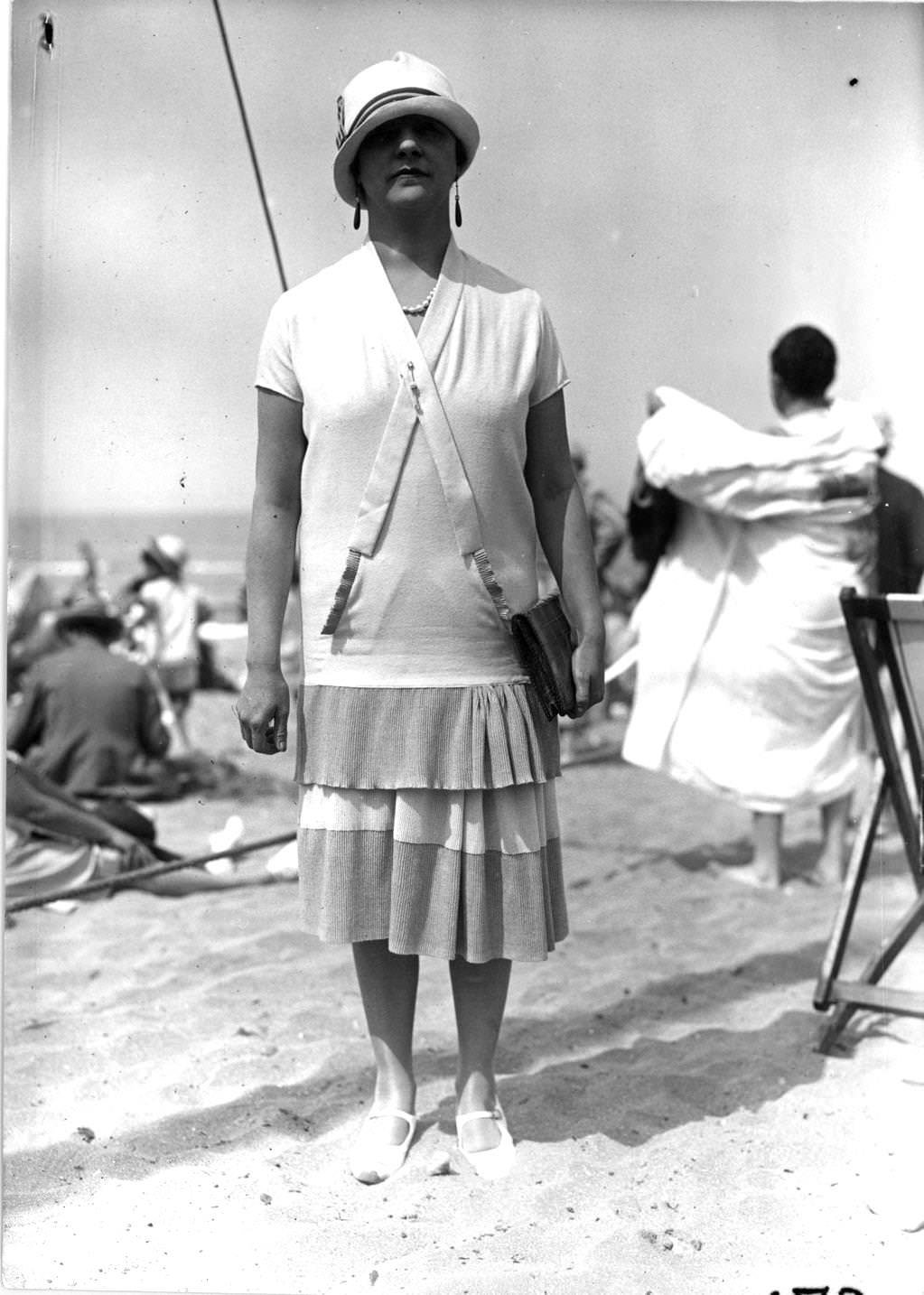 Single-flounce tunic dress with gathers over the hip worn with a small-brimmed cloche hat and drop earrings, 1926