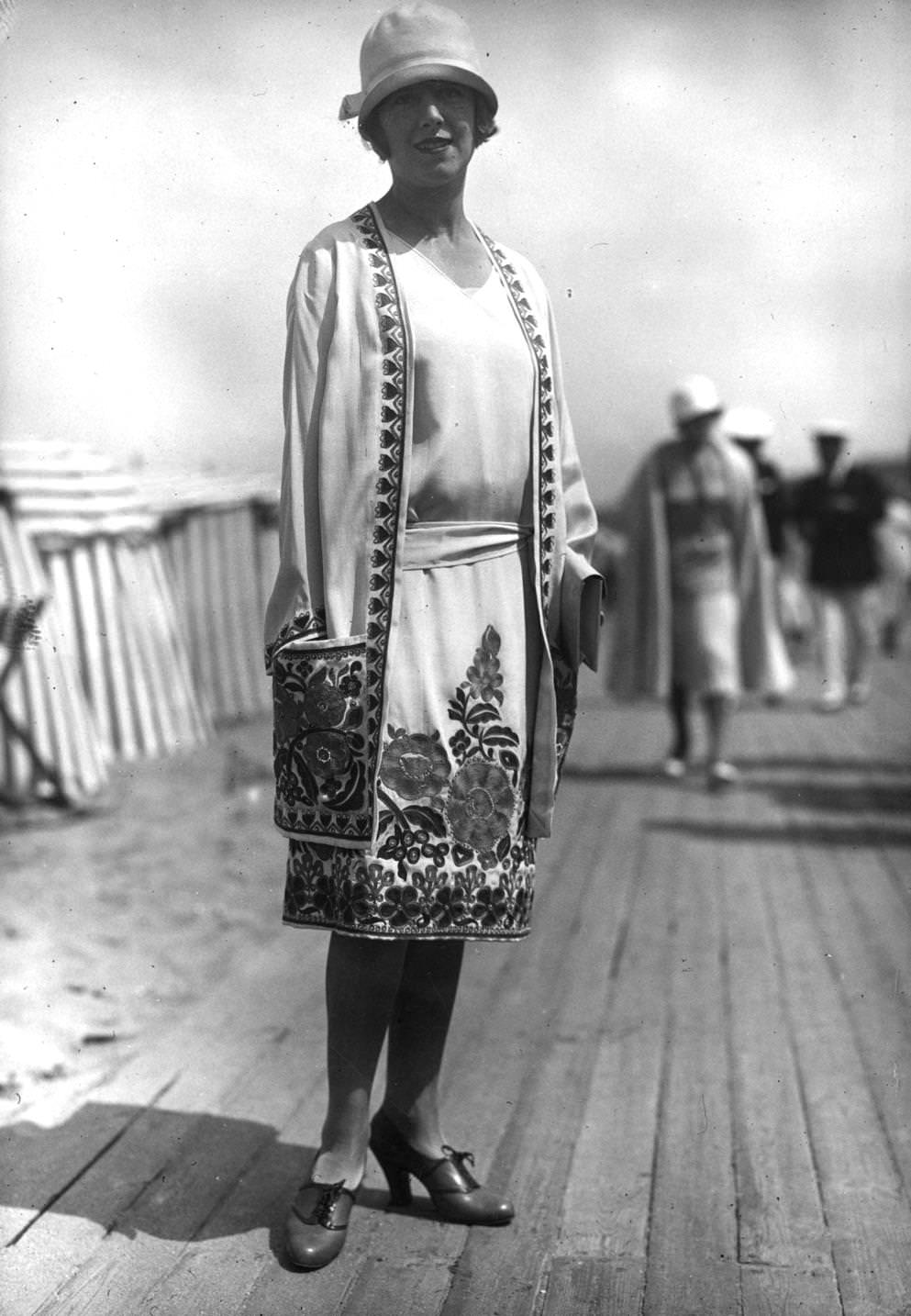ummer outfit designed by Nicole Groult. A matching dress and three-quarter coat have flower embroidery round hems and on pocket. Outfit is completed with a cloche hat and lace-up court shoes, 1926
