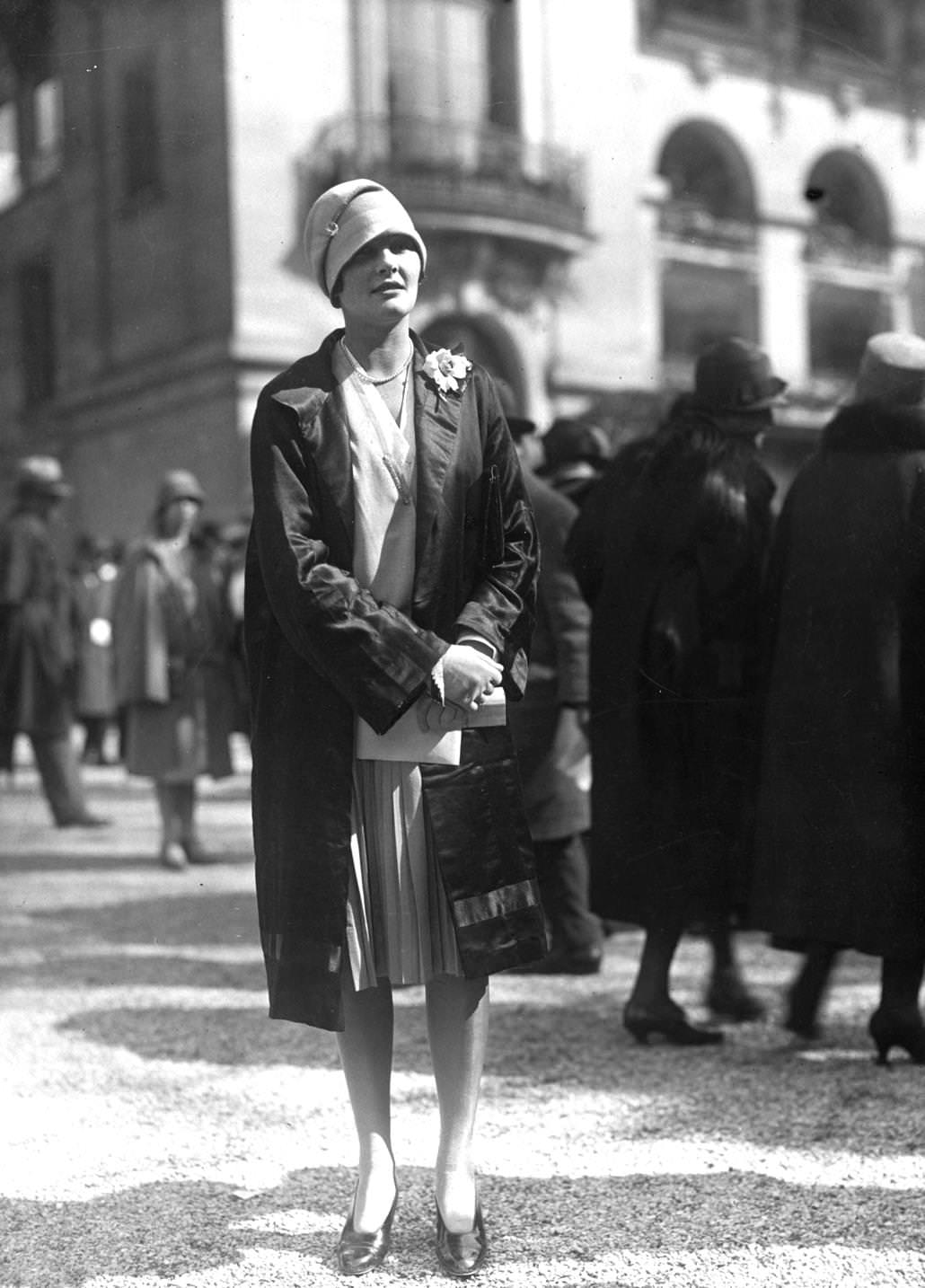 Folded cloche hat worn with a loose coat over a pleated skirt and v-necked blouse, 1926