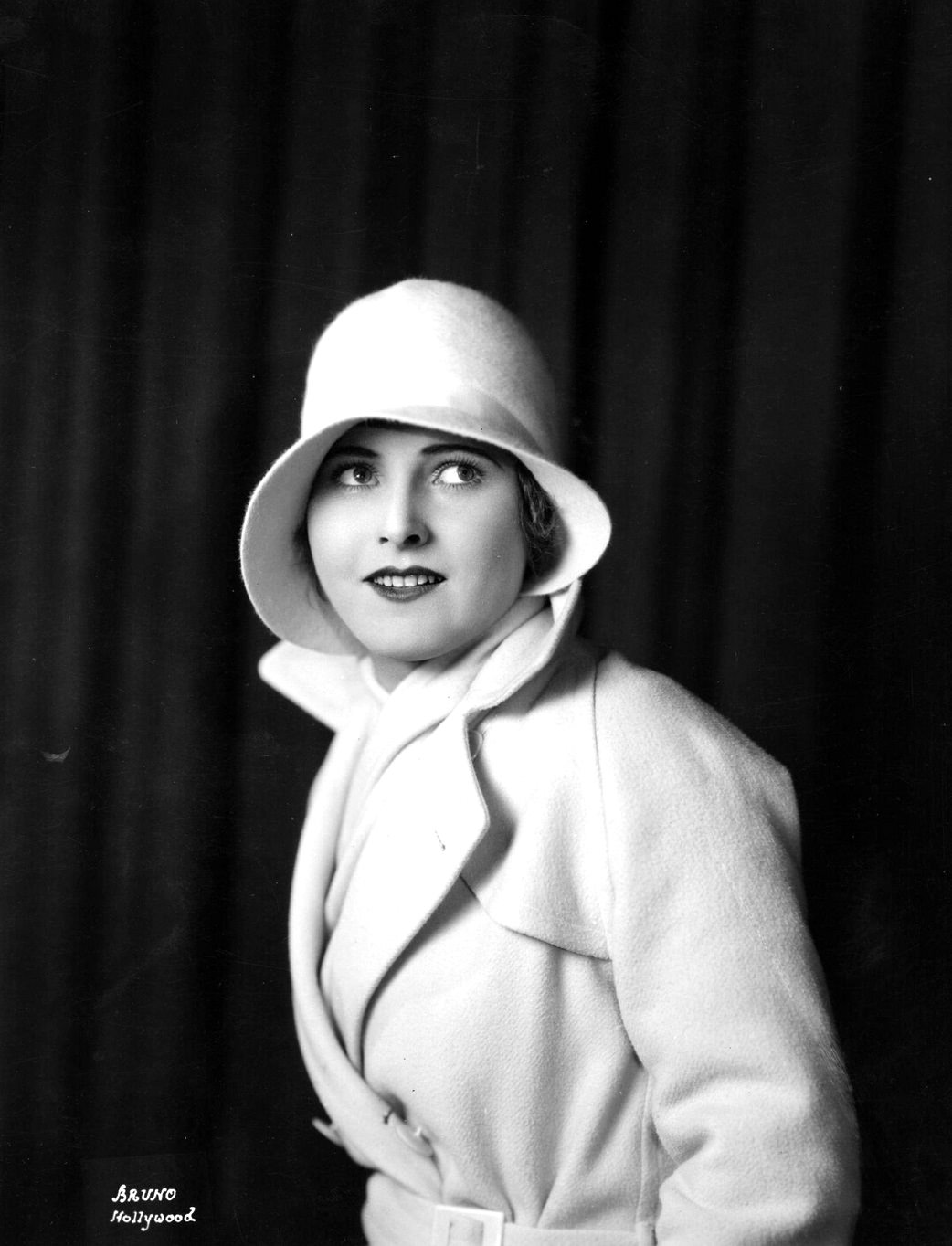 A half-length portrait of Lois Moran. She wears a white coat and cloche hat, 1920s