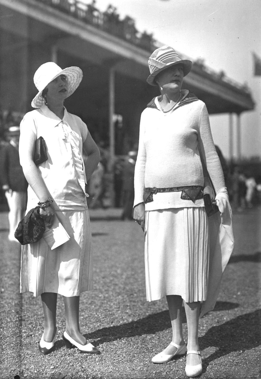 Two models wearing fashionable white outfits and cloche hats, inspired by sports designs during a day at the races, 1925