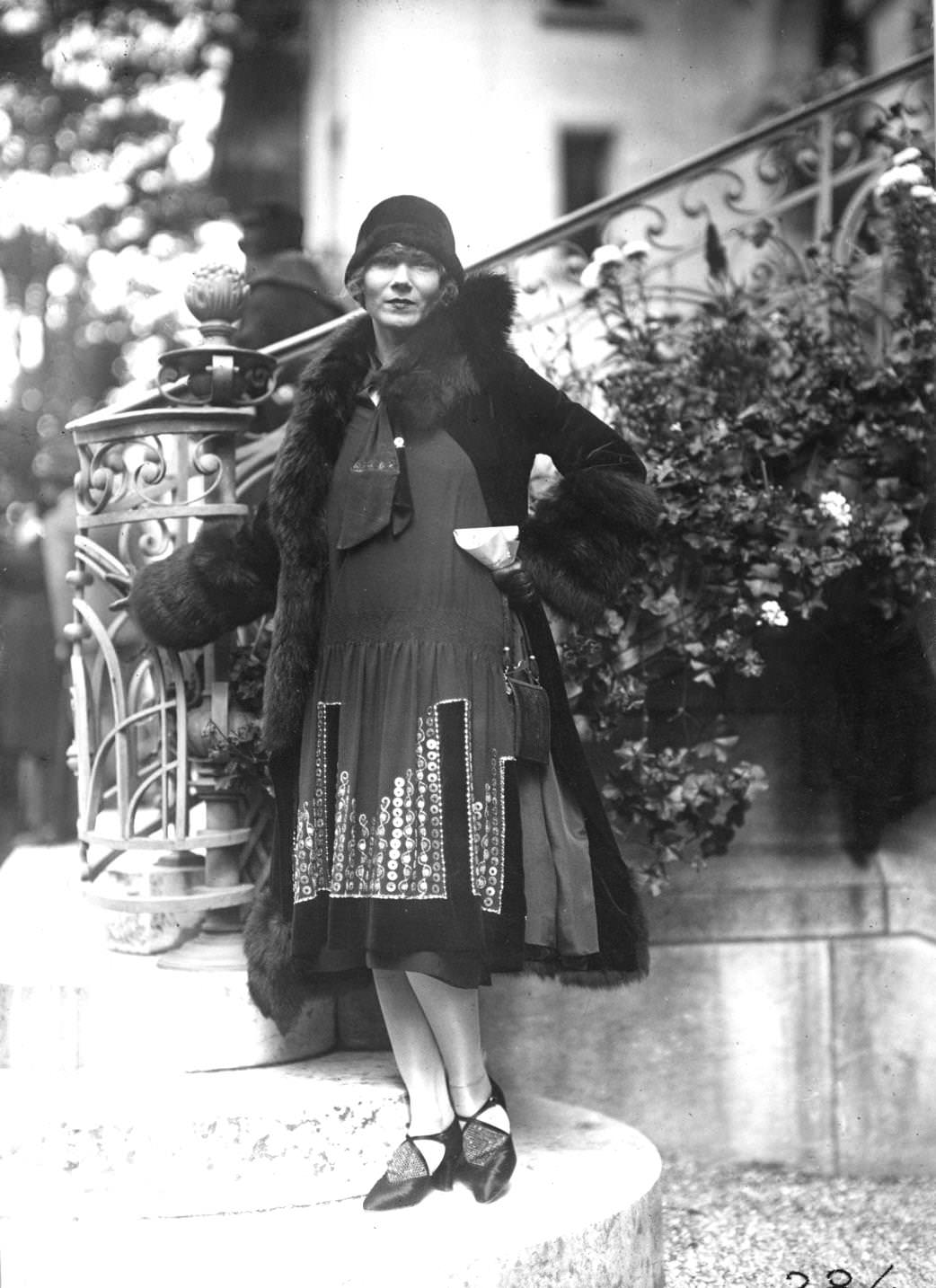 Tunic dress edged with embroidery worn under a coat edged with a heavy band of fur. Outfit designed by Lucien Lelong. Worn with a small cloche hat and shoes with a decorated vamp, 1925