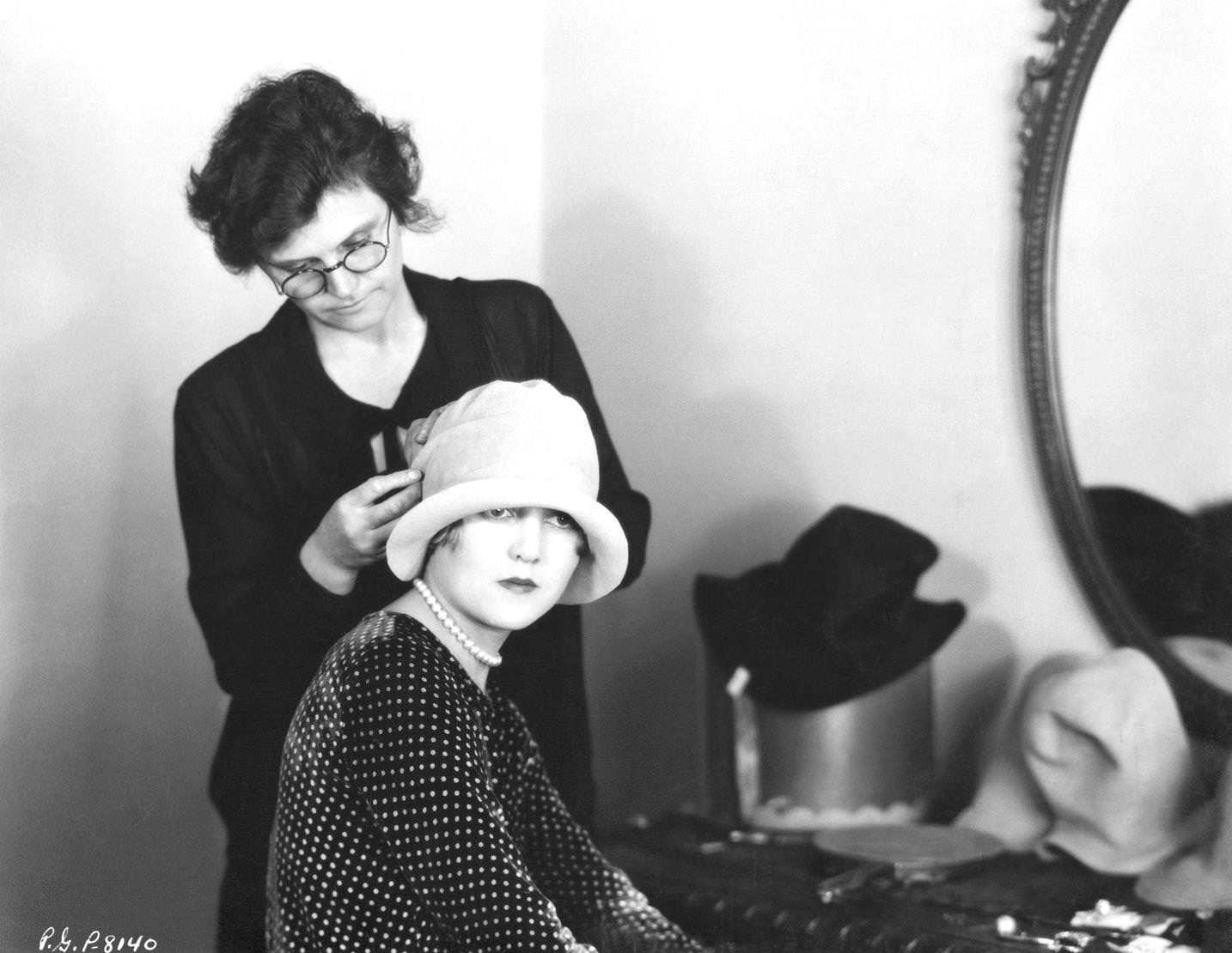 Wardrobe mistress adjusting actress Ruth Taylor's brimmed felt cloche hat, 1920s