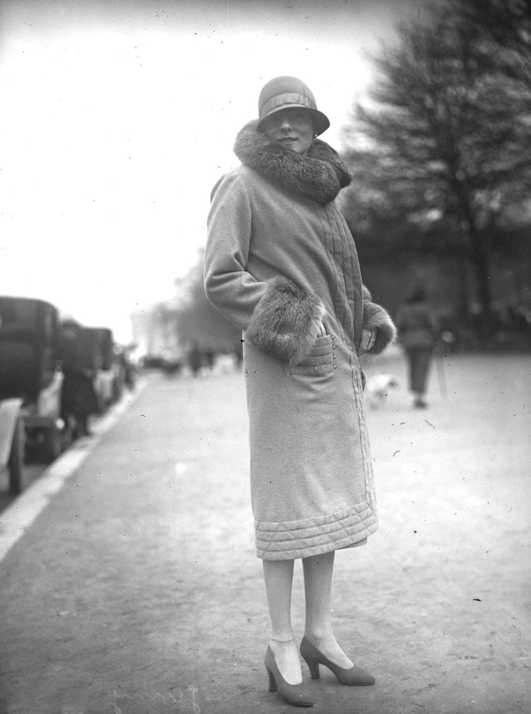 A model wearing a coat with a large fur collar and cuffs and a close fitting cloche hat, 1925