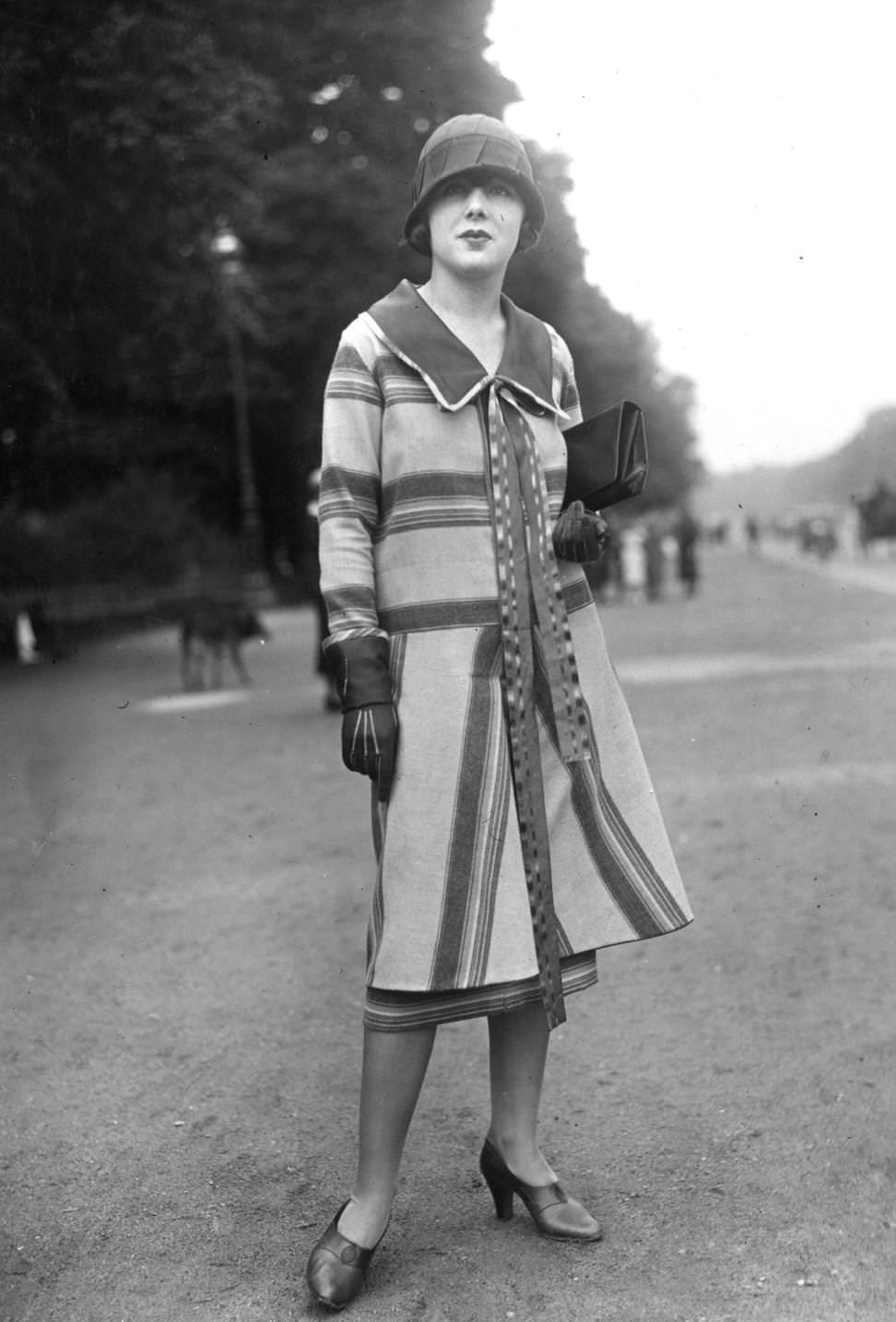 Striped coat with wide collar. Cloche hat, clutch bag, gauntlets and high vamp court shoes complete an outfit designed by Jane Laffitte, 1925