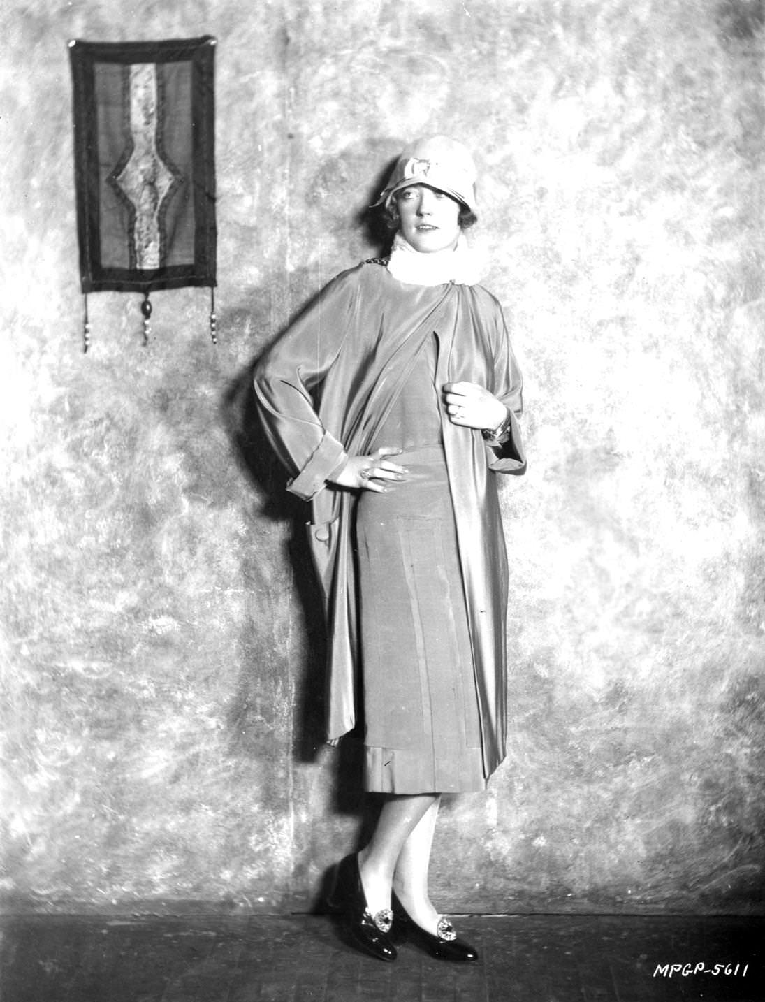 American film star Marion Davies modelling a cloche hat and a long jacket, 1920