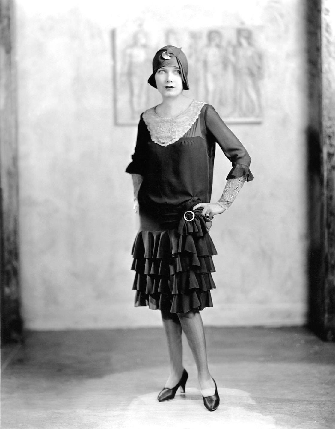 Young woman in a 'flapper' dress and cloche hat posing for portrait with hands on hips, 1922