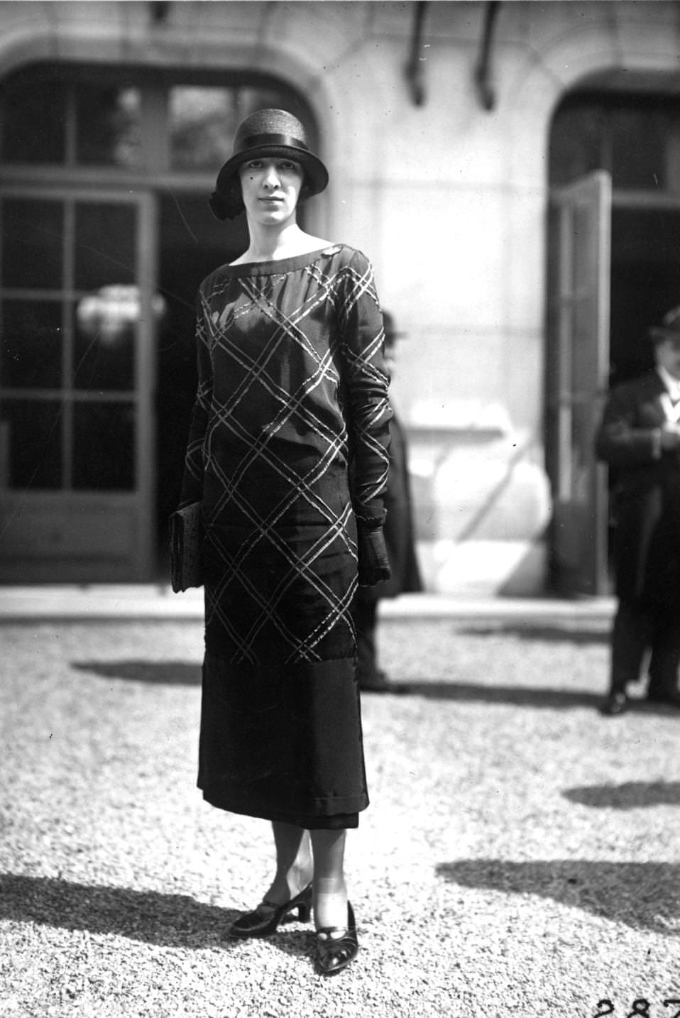 A long-sleeved collarless boat-necked tunic dress worn with a deep crowned cloche hat, 1924