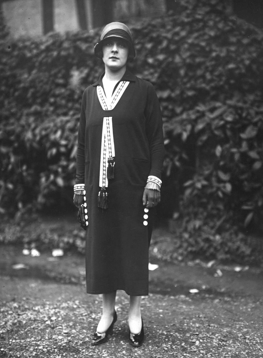 A model wearing a dress with a lace stream resembling a tie across its breast and cloche hat, 1924