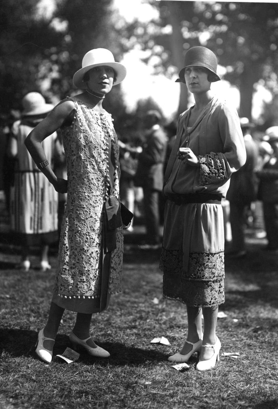 A long sleeveless overdress of lace and a drop-waisted long sleeved tunic dress with lace inserts worn with a cloche hat, 1924