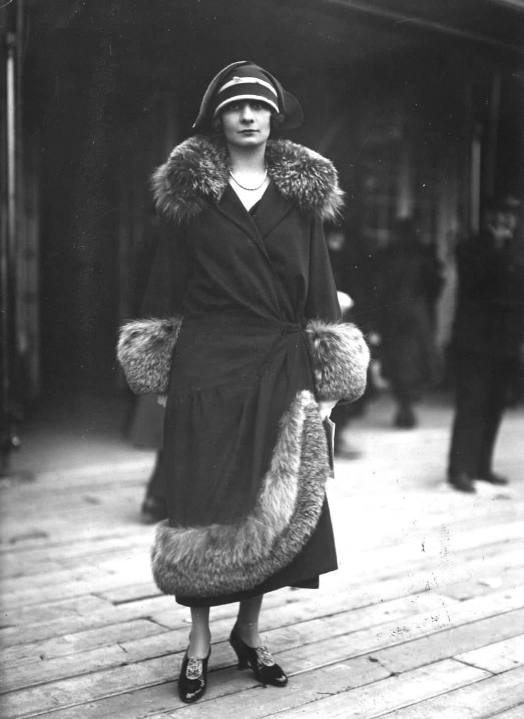 The model wears a fur trimmed coat which buttons at the side and cloche hat, 1923