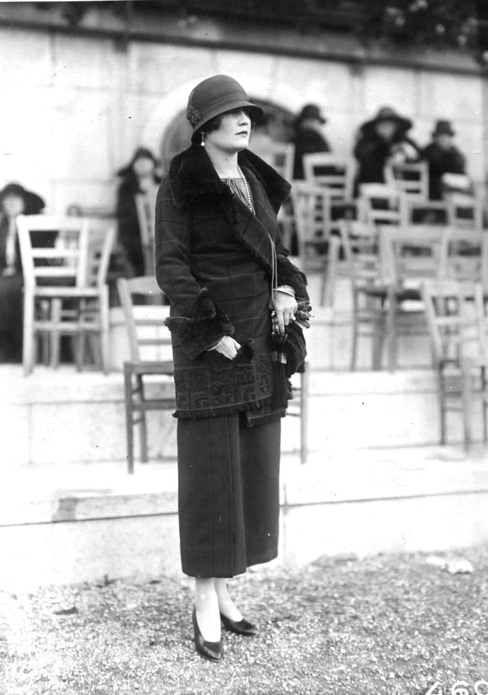 A tailored three quarter length jacket trimmed with fur on lapels and cuffs is worn over an ankle-length skirt. A cloche hat completes the ensemble, 1923