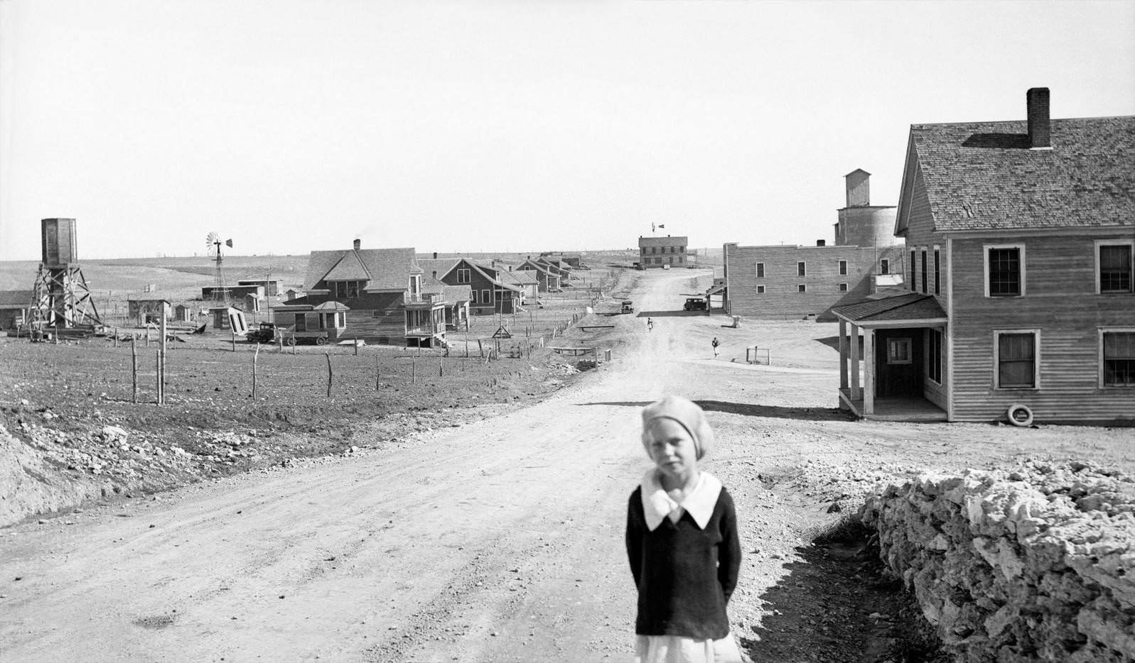Portrait of Young Girl, Street Scene with Abandoned Grain Mill and Bank both right in Background, Mills, New Mexico, 1930s