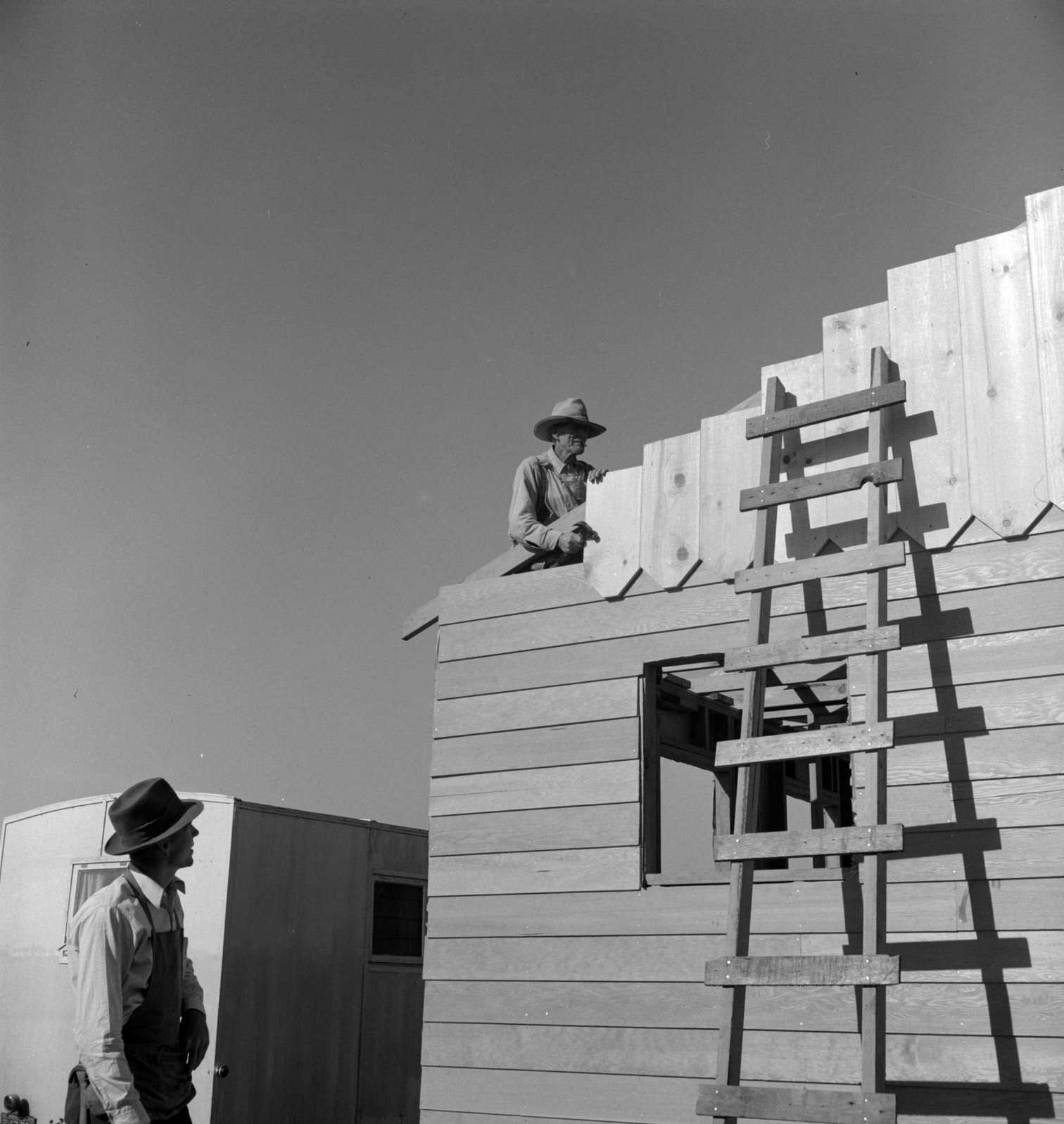 Father and son, recent migrants to California, building house in rapidly growing settlement of lettuce workers on fringe of town, 1930s