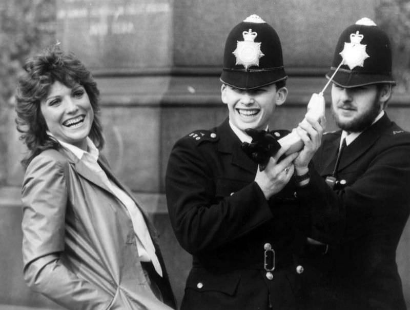 British actress Suzanne Danielle sharing a joke with two policemen while they examine one of the then-newly legal mobile phones in the United Kingdom, 1983.