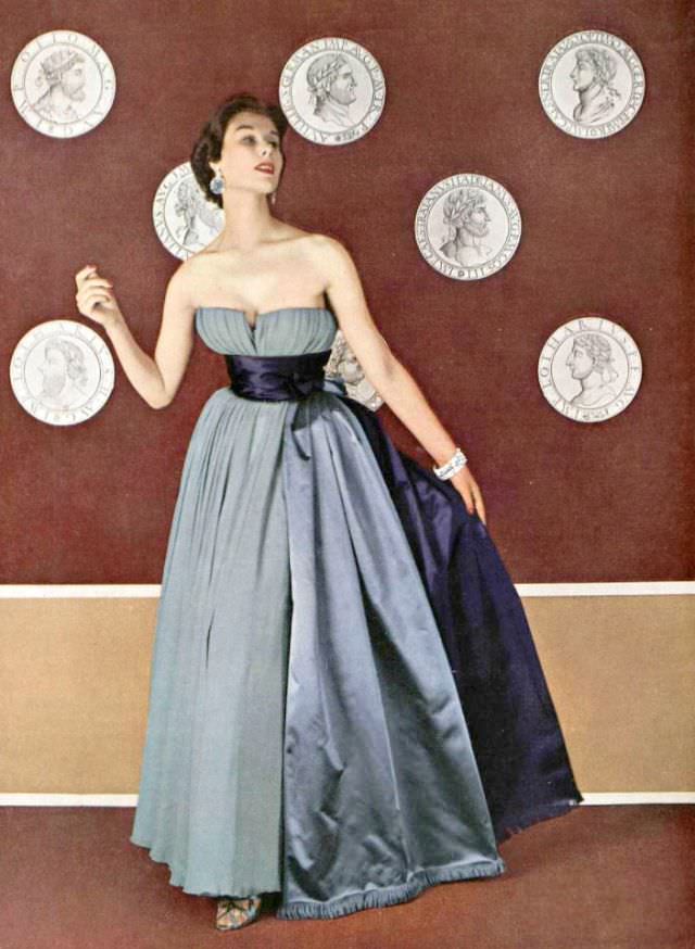 Myrtle Crawford in pale mauve chiffon evening gown, wide satin bands in two tones of purple extend to the floor, by Jacques Fath, 1953