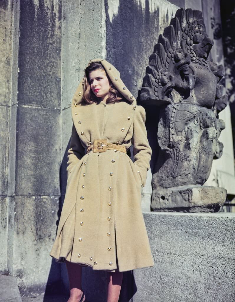 A female fashion model wears a camel wool coat in beige with leather belt and gilt buttons, part of the new collection from French couture designer Jacques Fath in Paris, France, 25th October 1945.