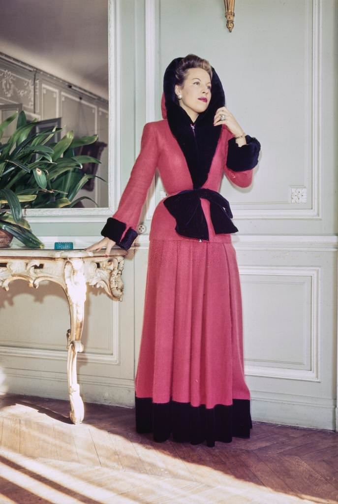 A female fashion model wears a home gown of Angora jersey in red with matching hood, both trimmed with black rabbit, part of the new collection from French couture designer Jacques Fath in Paris, France, 25th October 1945.