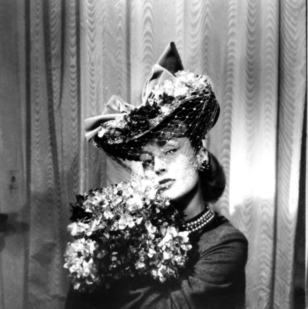 Woman wearing a hat with a veil, holding a bouquet of flowers, Paris, 1943.