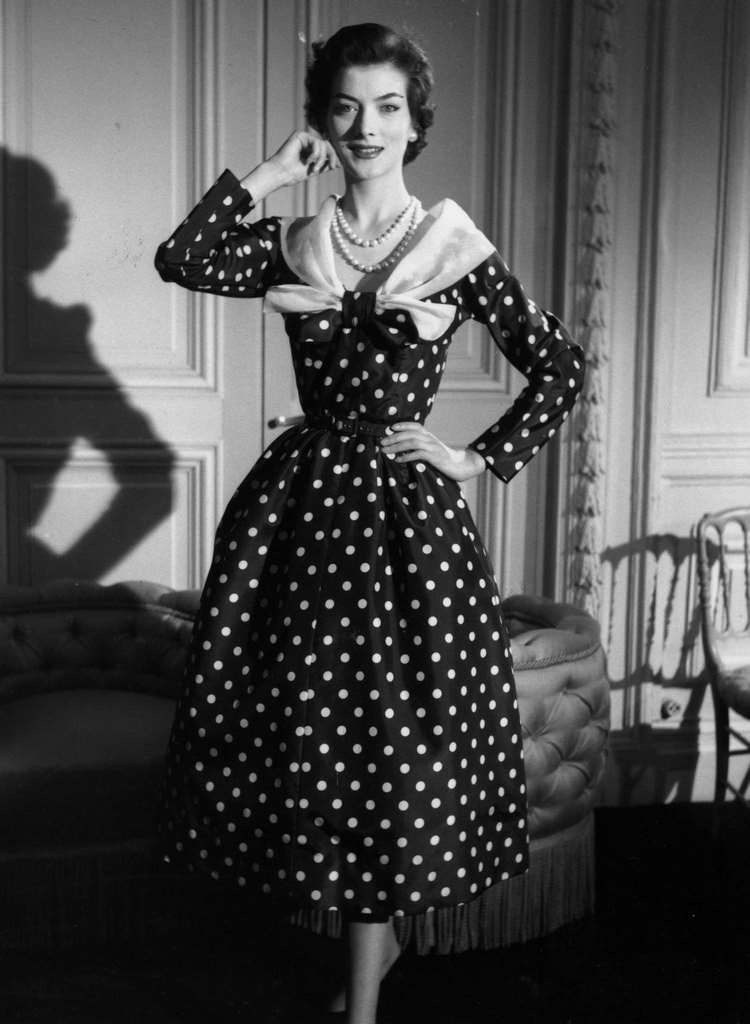 A 'ready-made' afternoon dress designed by Jacques Fath, polka dotted with long sleeves, tight waist and muslin shawl collar. The House That Fath Built, 1955
