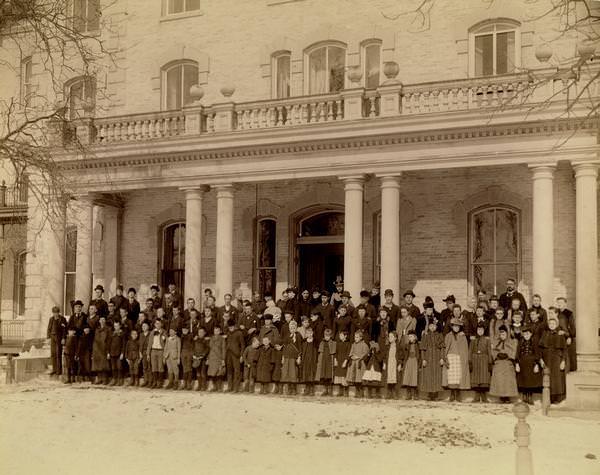 Students and adults of the State School for the Blind pose for a group portrait in front of the building, 1893