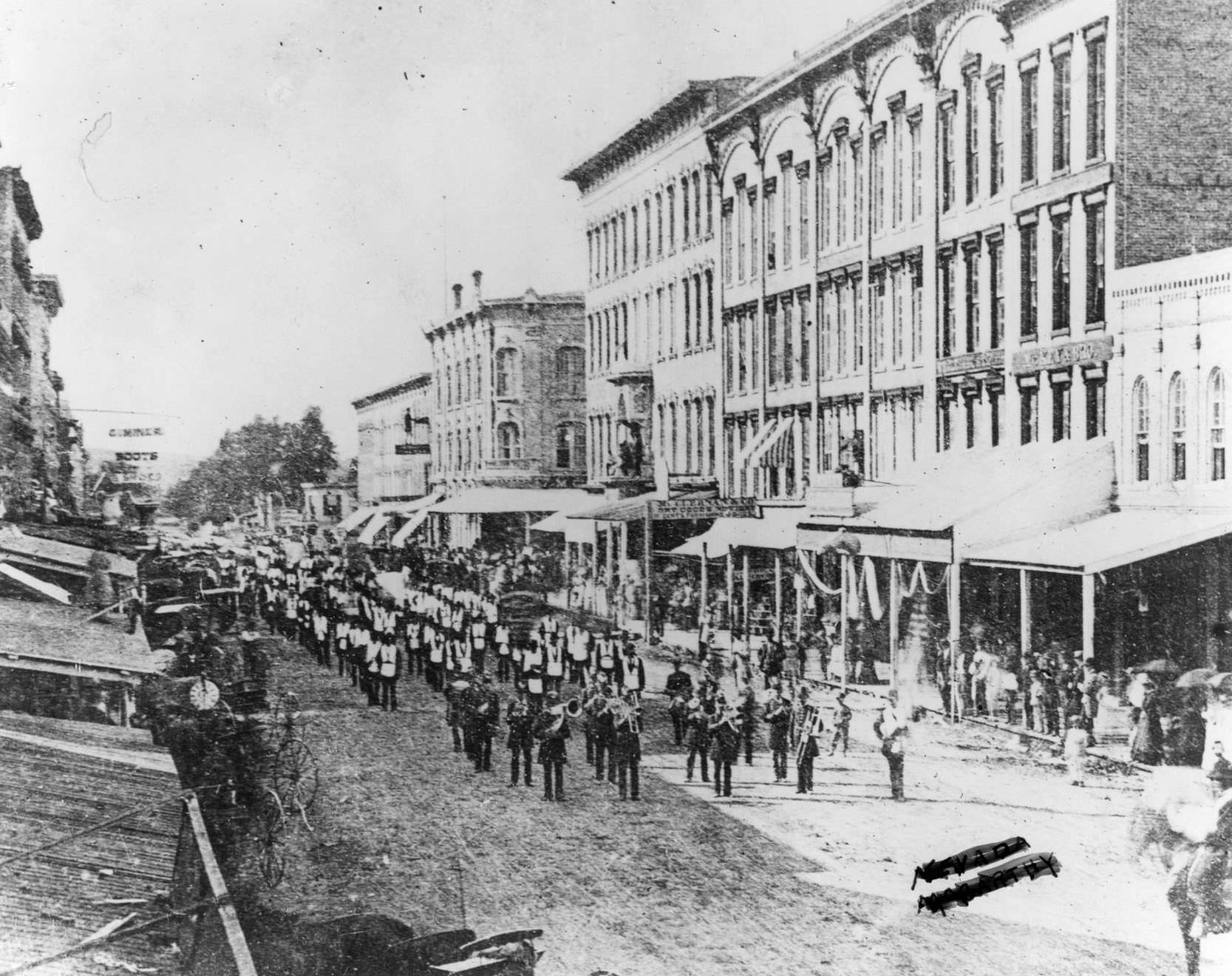 A marching band marching down Janesville's unpaved Main Street in a Fourth of July parade, 1869.