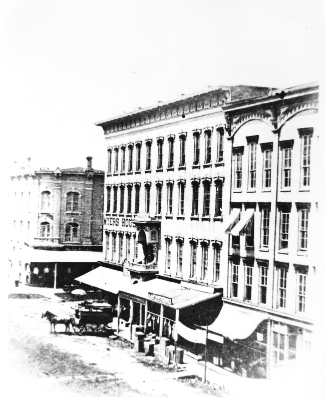 Myers House Hotel from South Main Street. Photo includes an unpaved street, a horse and coach, 1875