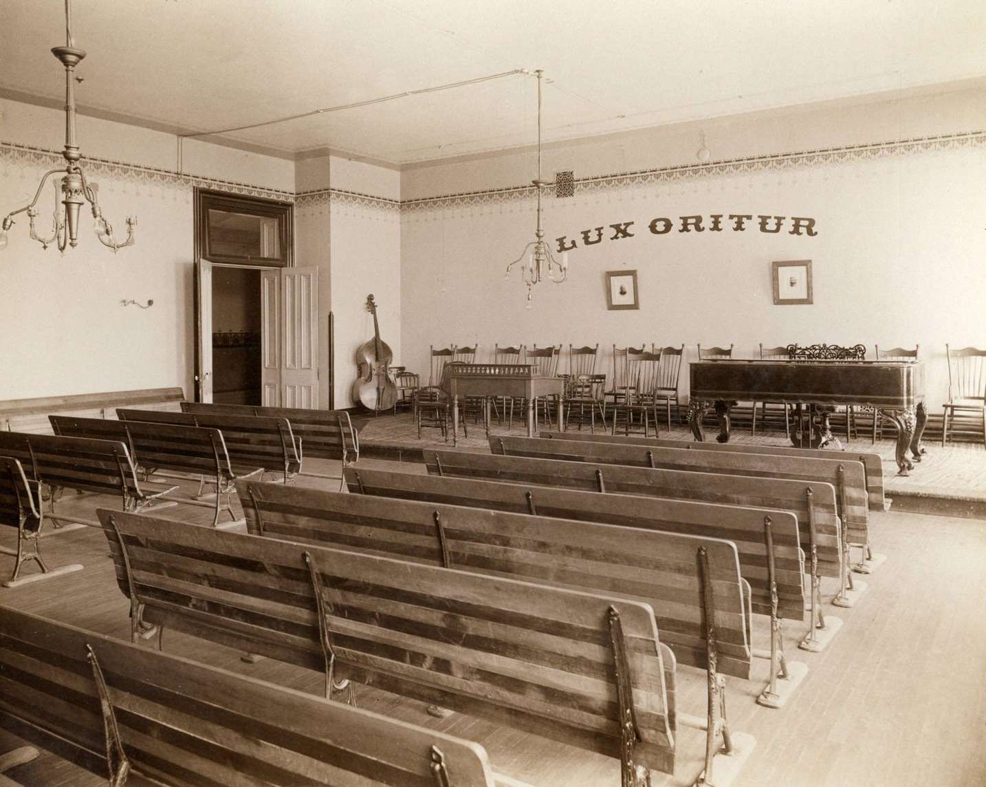 Music recital room at the State School for the Blind with seven rows of seating, a piano and cello, Janesville, Wisconsin, 1893.